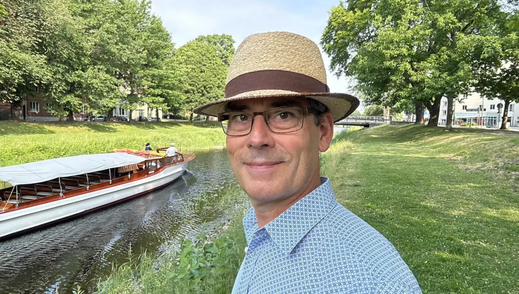 Sommarhälsning 2023: Peter står vid älven i Karlstad i sommarhatt